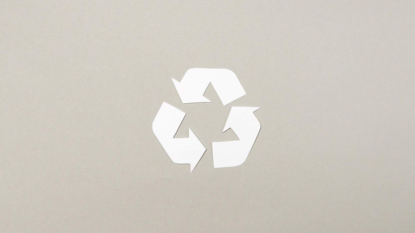 Simple paper cutout recycle symbol on a neutral gray background, emphasizing sustainability.